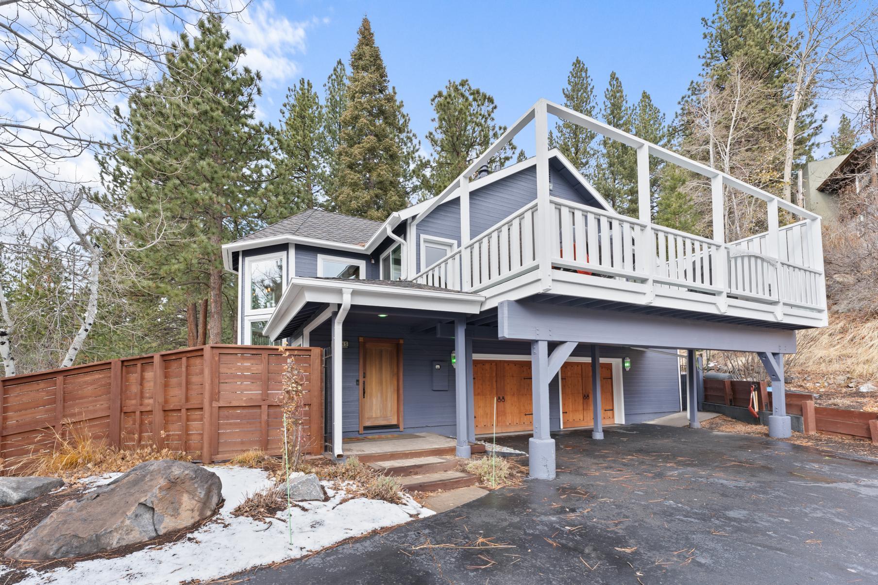 Two-story vacation rental in Truckee with large balcony, surrounded by trees and a wooden fence, on a clear winter day.