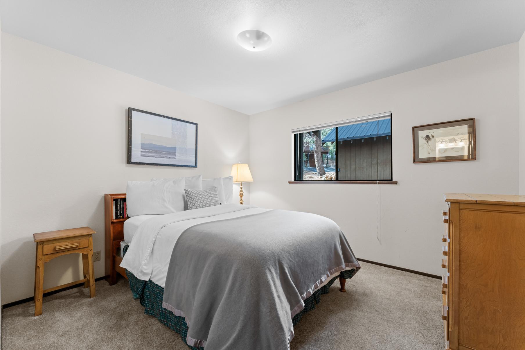 Cozy bedroom in a Truckee vacation rental, featuring a comfortable bed, artwork, and window view of trees.