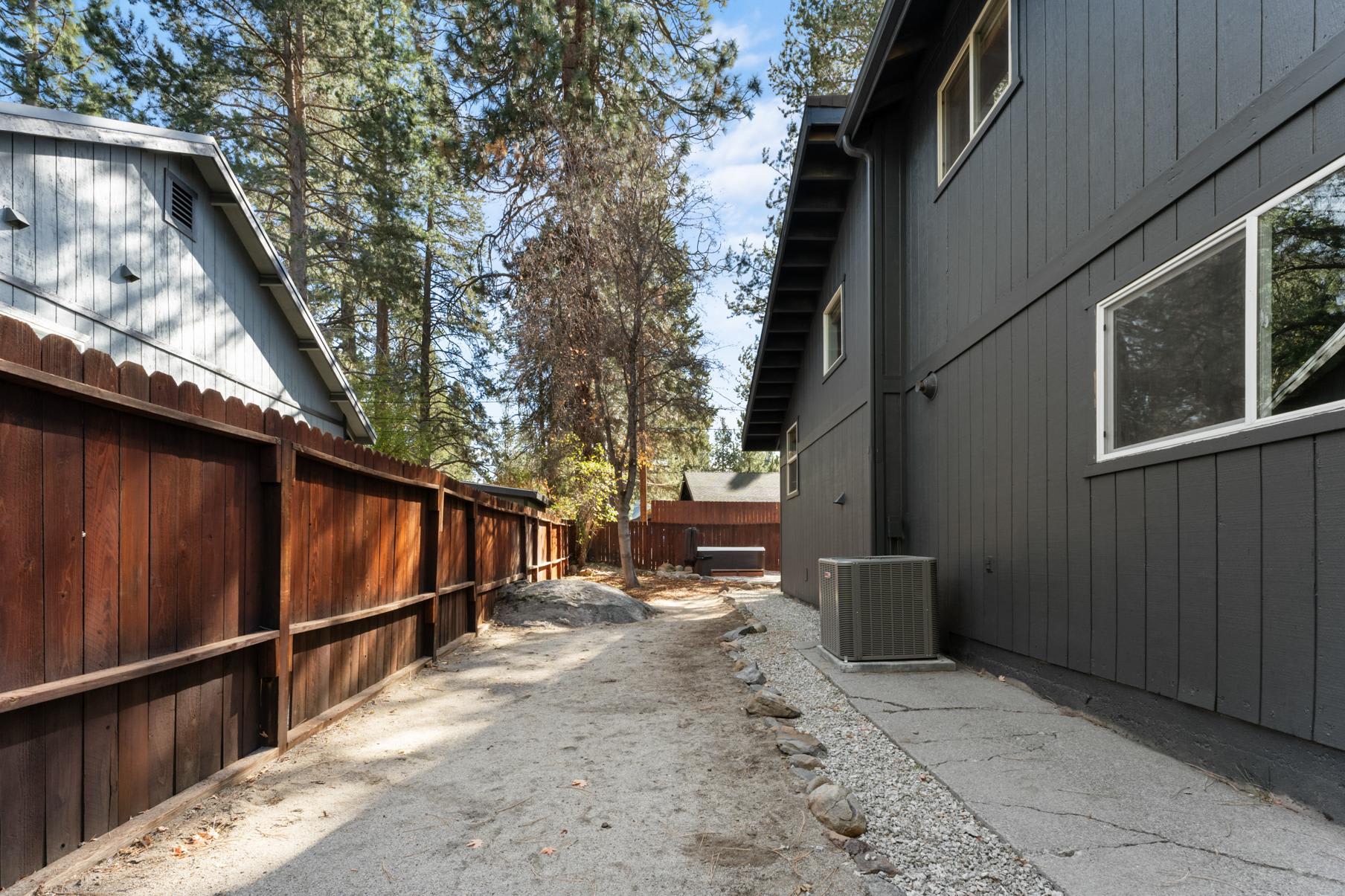 Side yard of a Truckee vacation rental with wooden fence, surrounded by tall trees and a visible hot tub at the back.