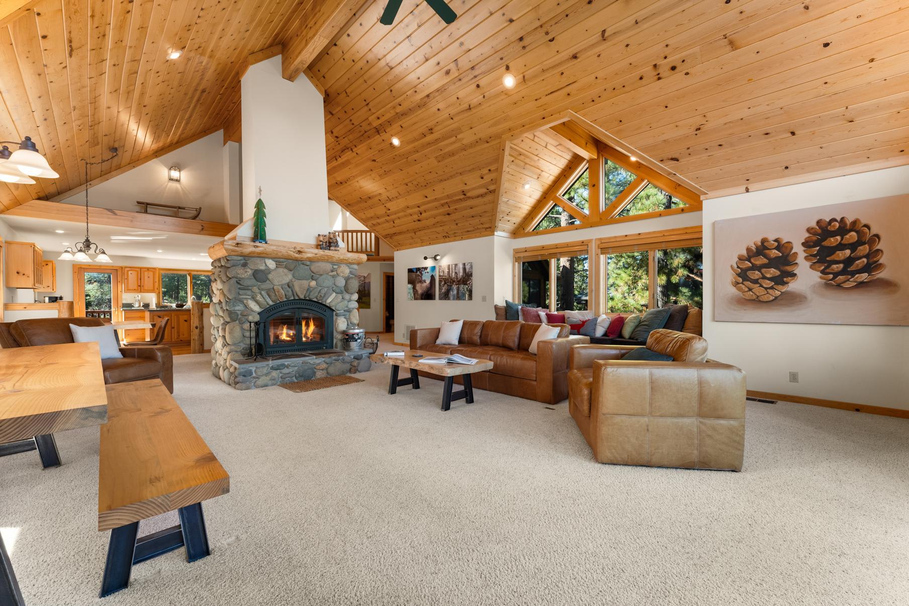 Spacious living room in a Truckee vacation rental with a stone fireplace, wooden ceiling, leather sofas, and large windows.