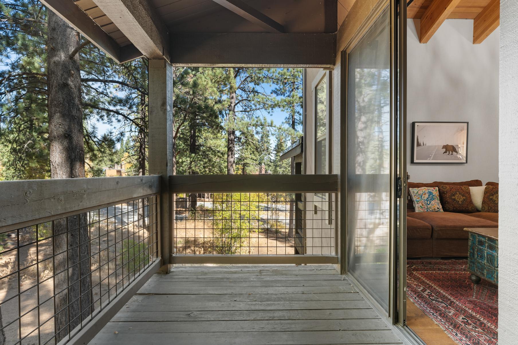 Balcony view from a cozy vacation rental in Truckee, overlooking pine trees and a rustic interior with a brown couch.