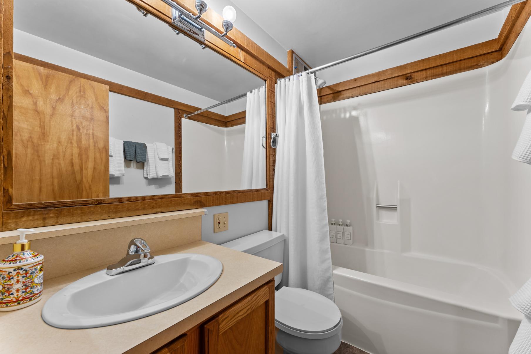 Bathroom in a Truckee vacation rental with wood accents, a sink, toilet, and a shower with a white curtain.