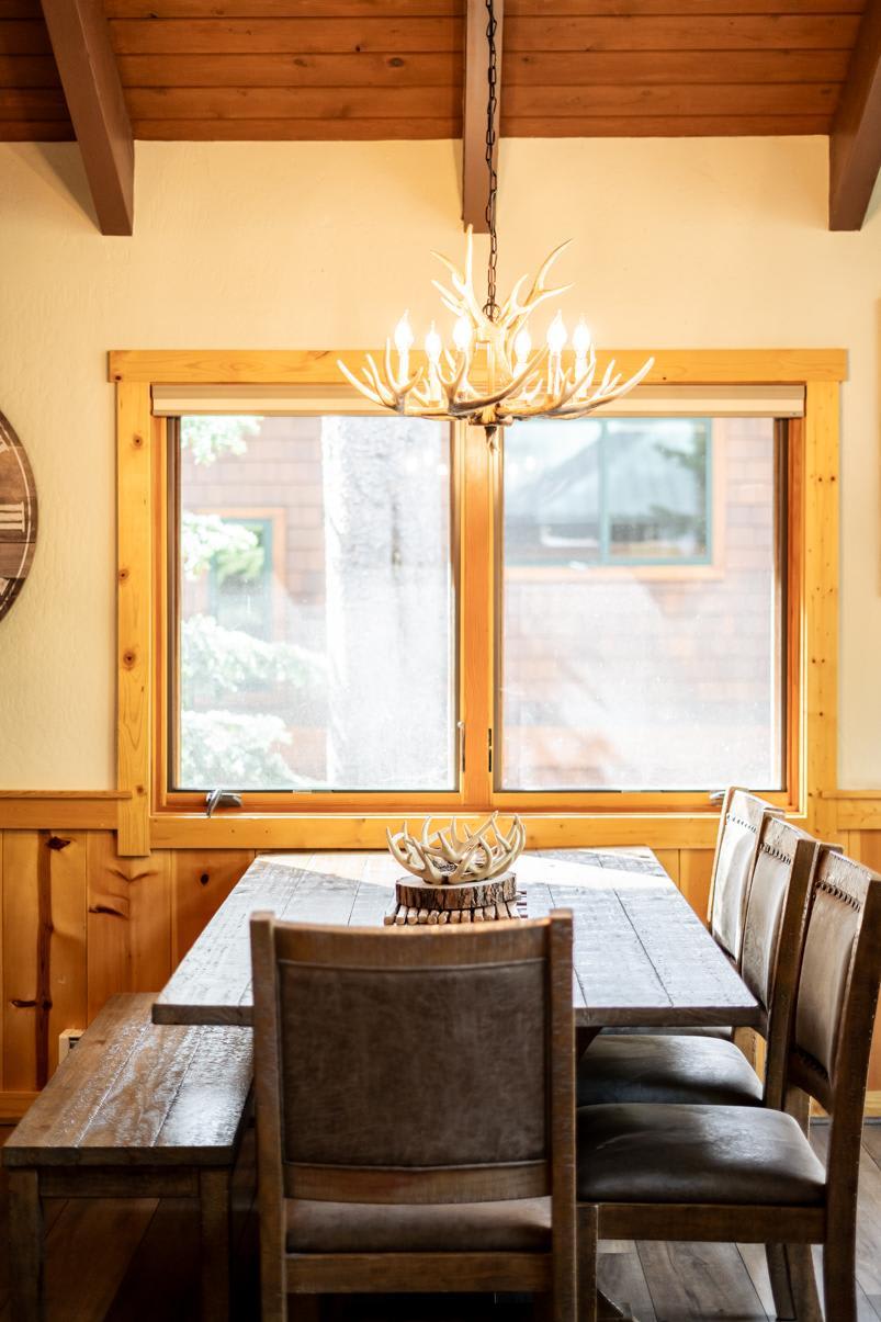 Rustic dining area in a Truckee vacation rental with wooden table, leather chairs, and antler chandelier by large window.