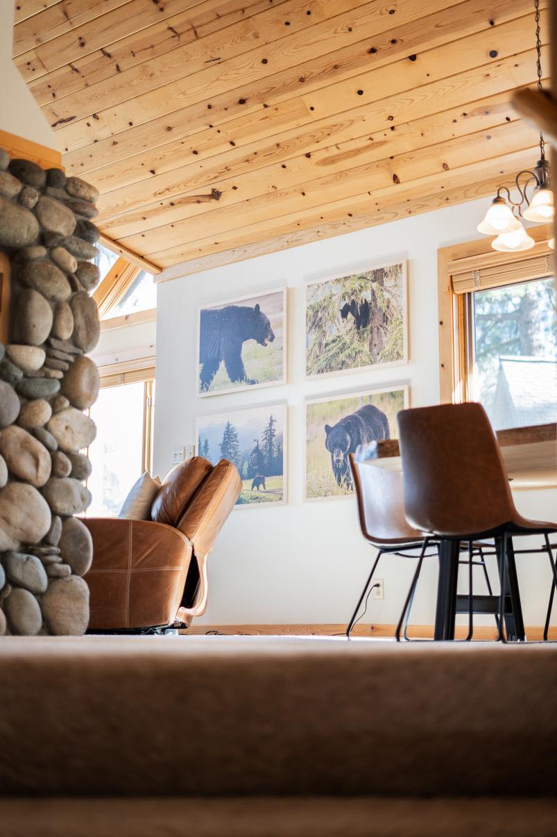 Cozy Truckee vacation rental with stone fireplace, leather chair, and bear artwork on walls near a wooden dining table.