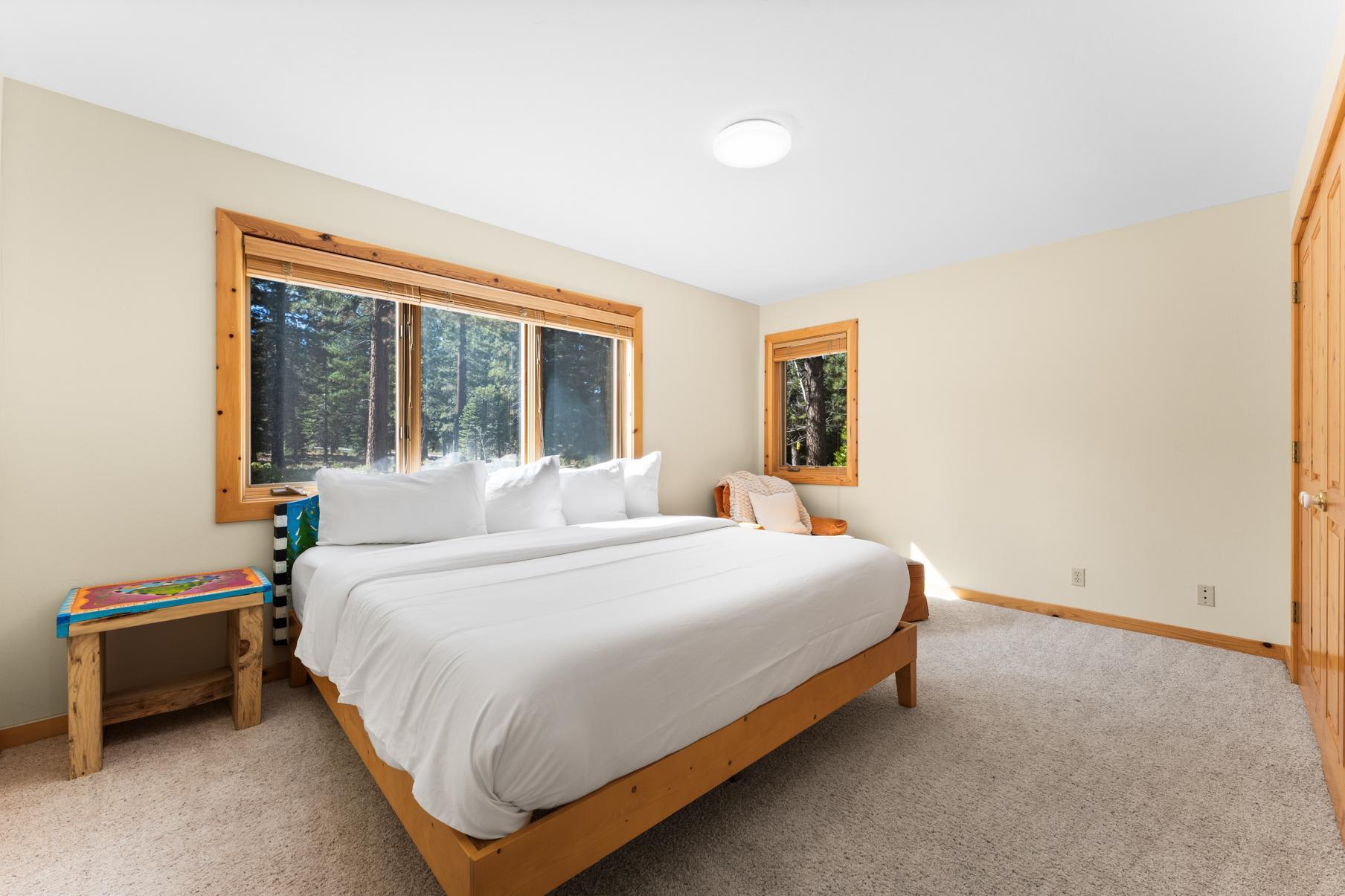 Bedroom with large bed in a Truckee vacation rental, featuring wooden accents and views of a forest through large windows.