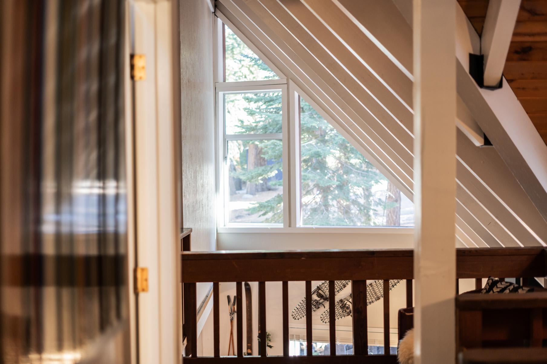 A-Frame window view in a Tahoe Vista vacation rental, framed by wooden beams and overlooking pine trees.