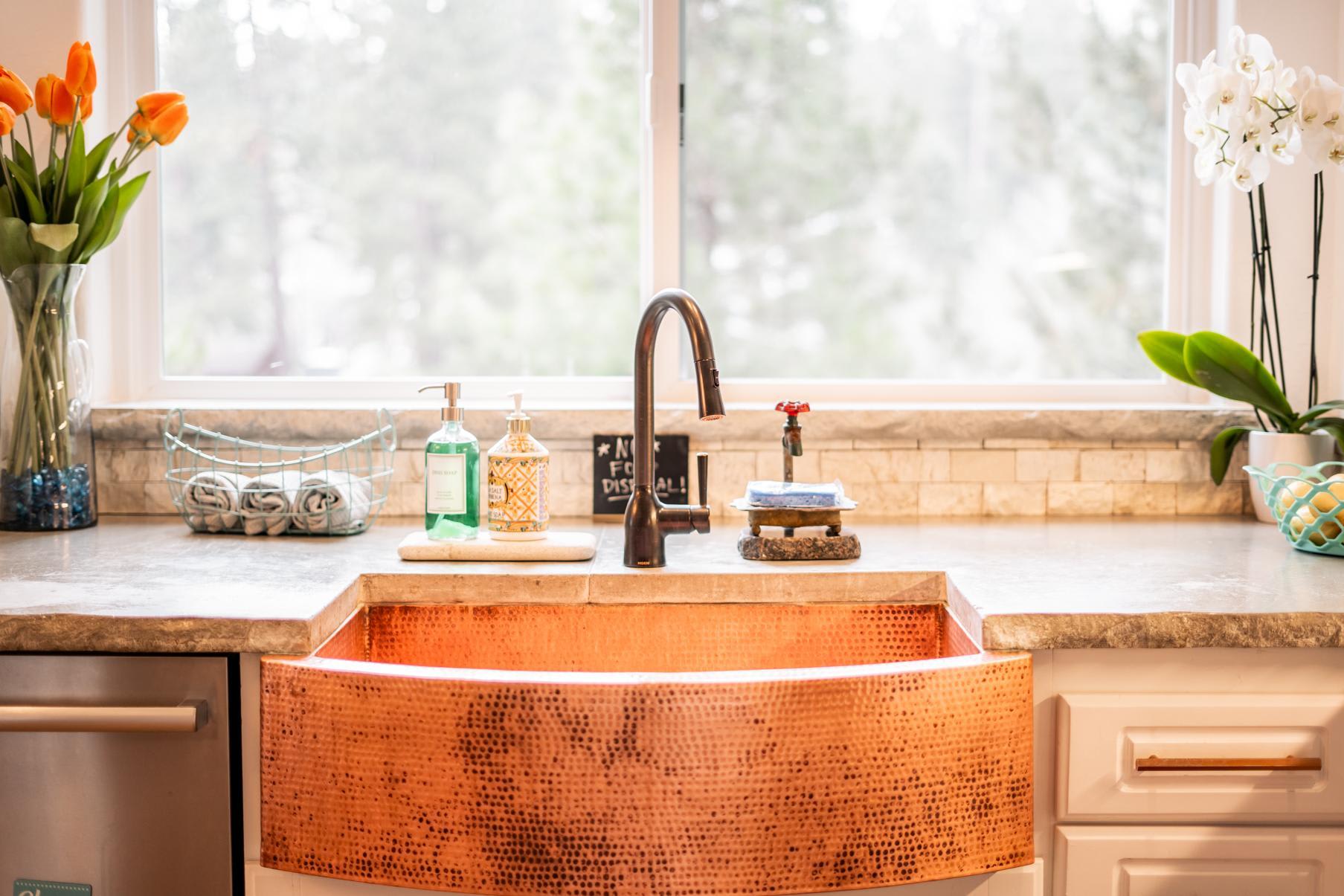 Stylish kitchen sink and decor in a Truckee vacation rental, with flowers on the counter and a scenic window view.