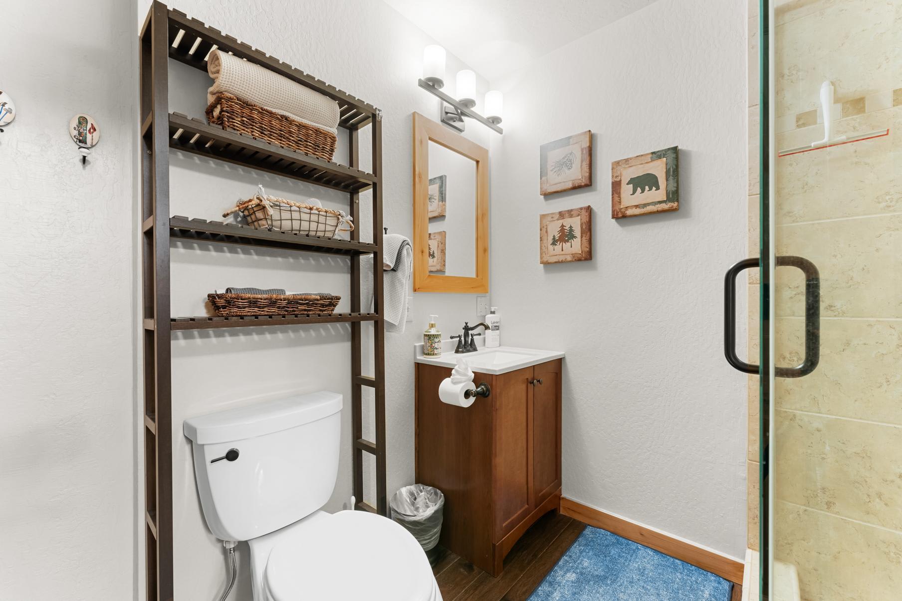 Bathroom in Truckee vacation rental with rustic decor, wooden cabinet, shelving, and framed nature-themed art.