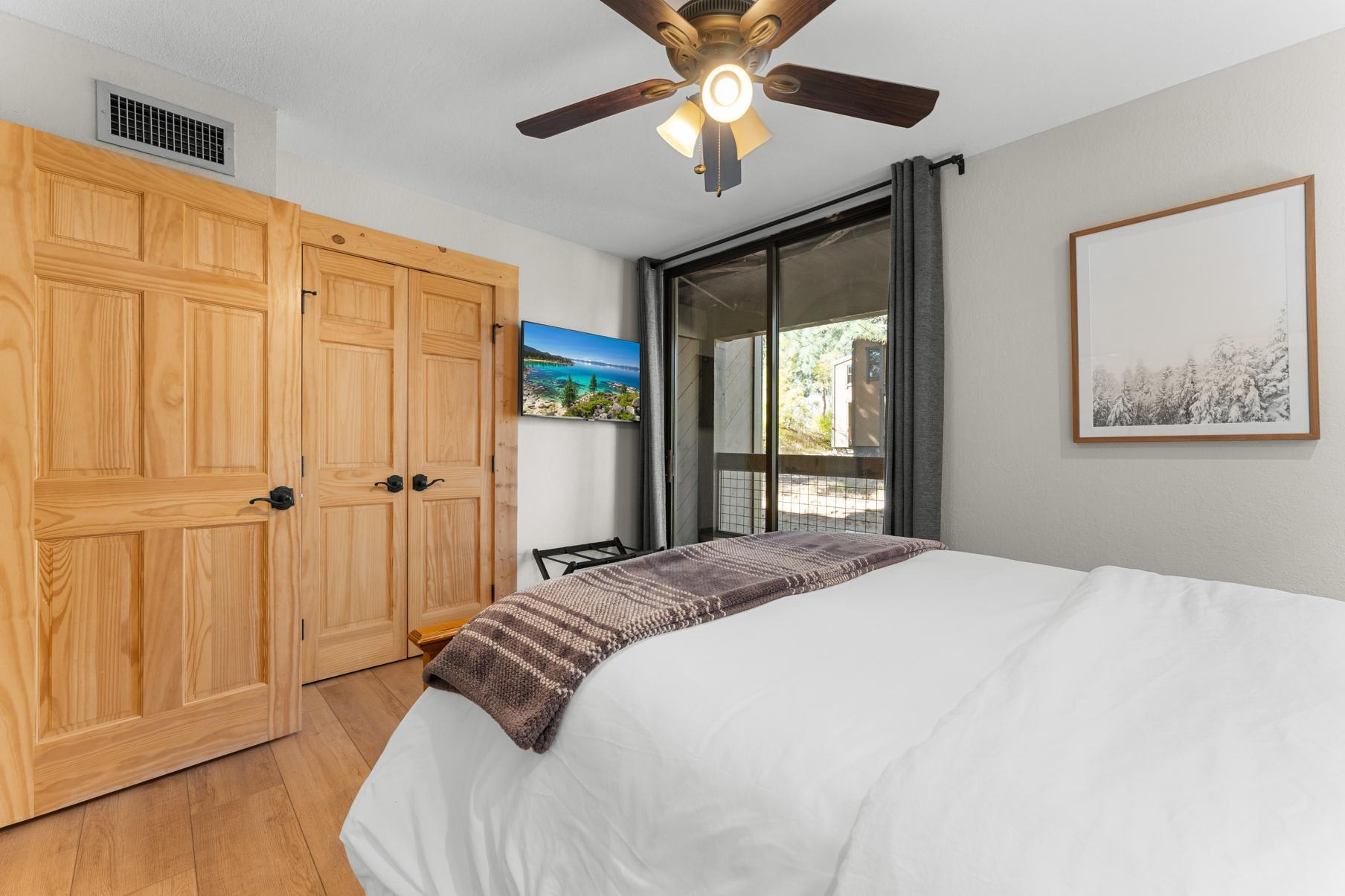 Cozy bedroom in a Truckee vacation rental, featuring a plush bed, wooden doors, ceiling fan, and a scenic view.