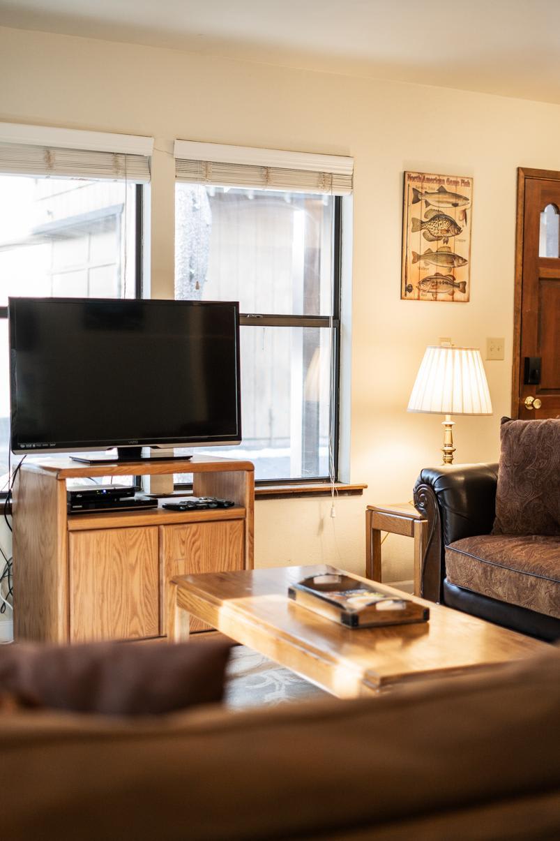 Cozy living room in Truckee vacation rental, featuring a TV, couch, lamp, and wooden coffee table with a relaxed vibe.