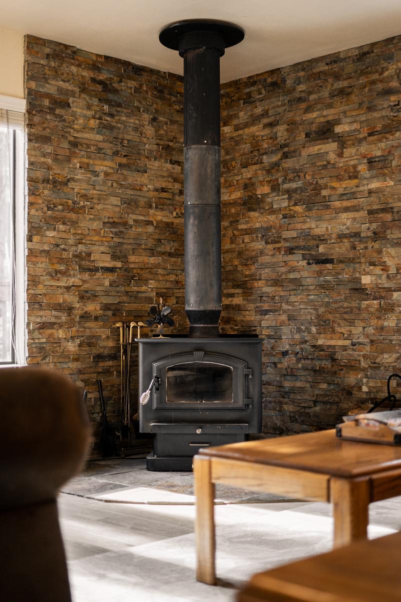 Cozy corner with wood-burning stove in a Truckee vacation rental, featuring rustic stone walls and wooden furniture.