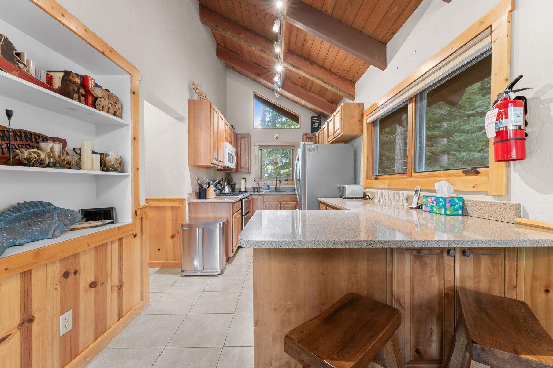 Cozy kitchen in a Truckee vacation rental with wood cabinets, vaulted ceiling, and nature view through large windows.