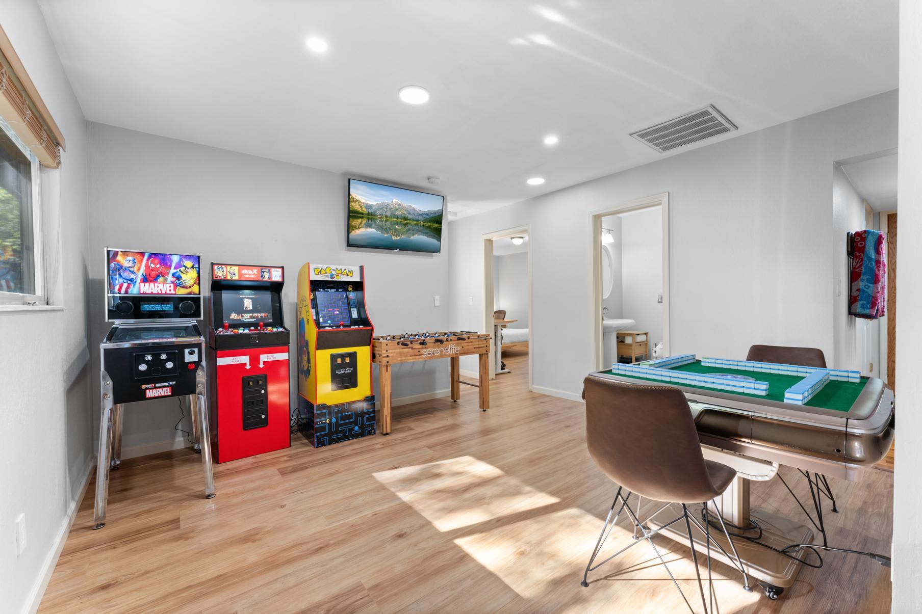 Game room in a Truckee vacation rental with arcade machines, foosball, and a mahjong table, featuring wood flooring.