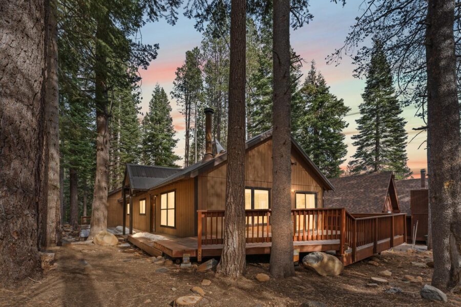 Cozy cabin vacation rental in Truckee, surrounded by tall pine trees at sunset with a wooden deck.