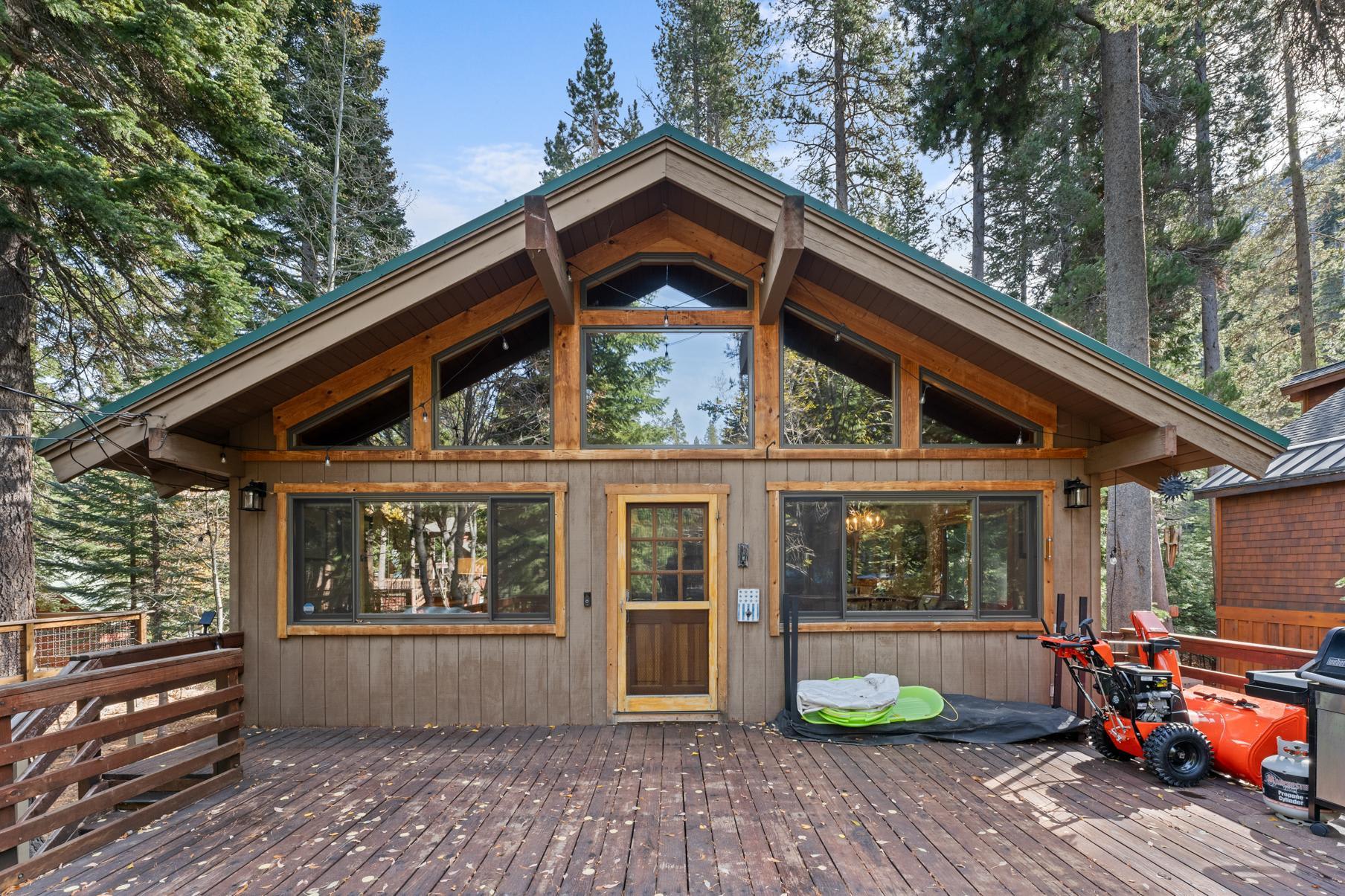 Cozy wooden cabin vacation rental in Truckee, surrounded by tall trees, featuring a spacious deck and large windows.