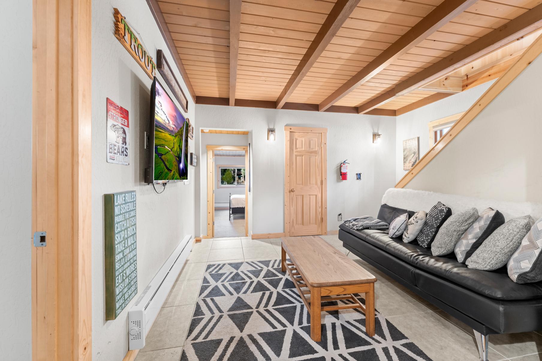 Cozy living room in a Truckee vacation rental, featuring a TV, patterned rug, and wooden accents with abundant natural light.