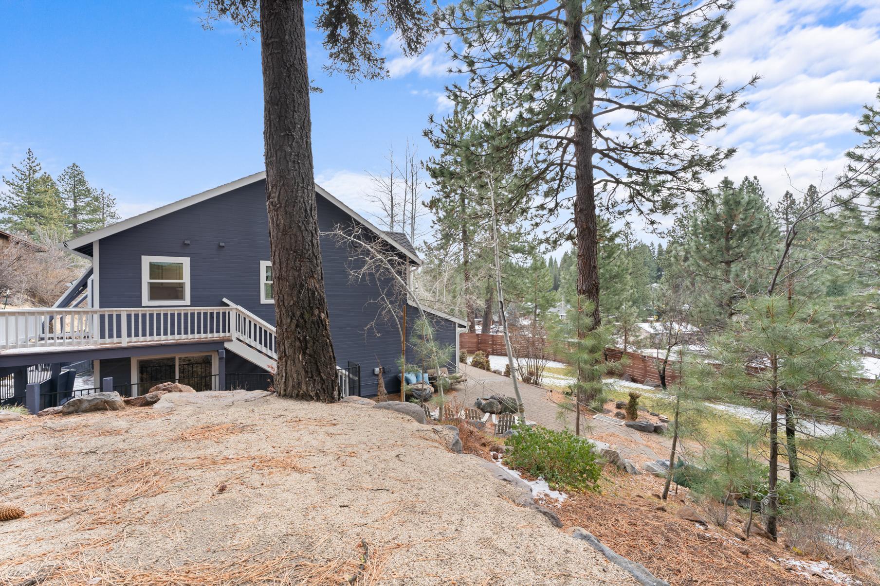 Blue house amidst pine trees, Truckee vacation rental with a spacious wooden deck overlooking a serene, forested landscape.