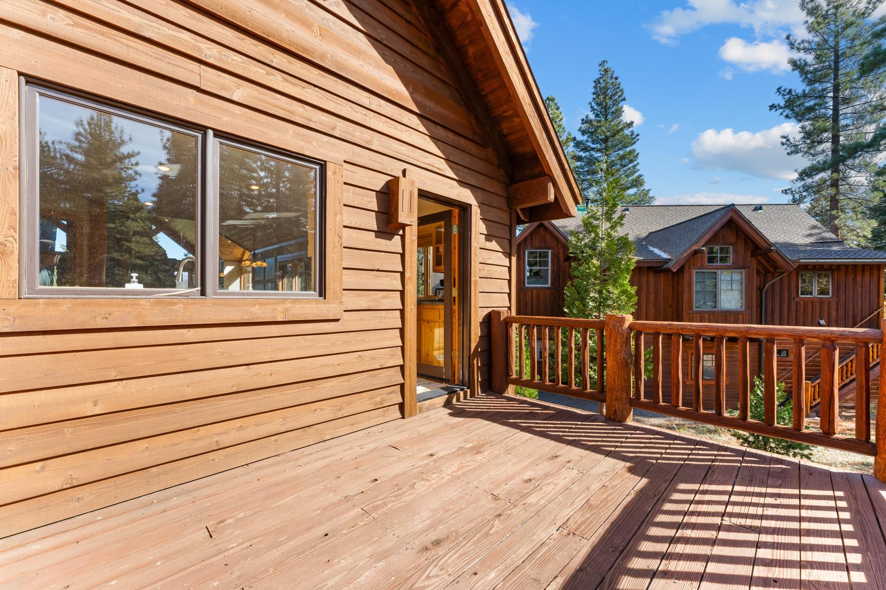 Wooden deck of a vacation rental cabin in Truckee, surrounded by pine trees and other rustic cabins.