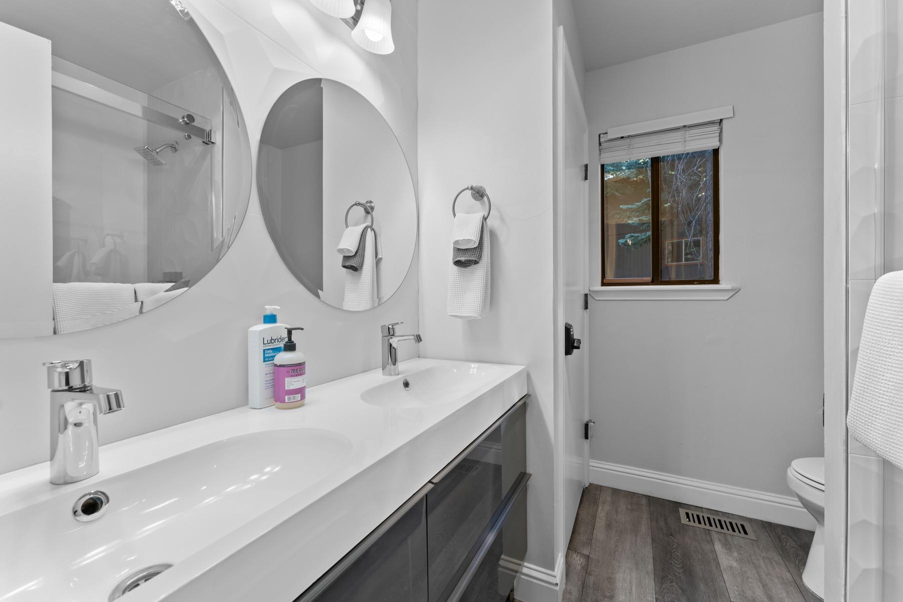 Modern bathroom in a Tahoe Vista vacation rental with a double sink vanity, round mirrors, and natural light from the window.