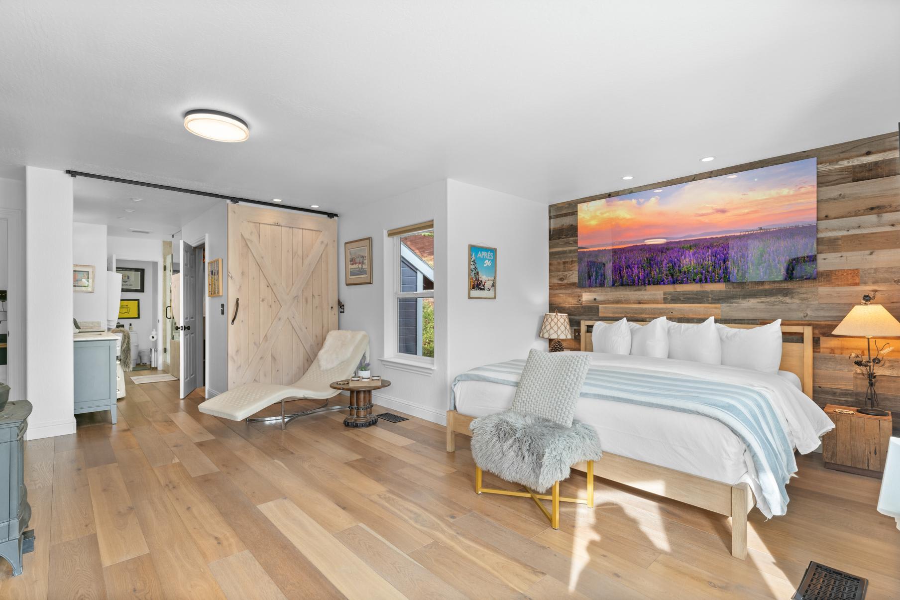 Spacious Truckee vacation rental bedroom with a wooden accent wall, cozy chair, and scenic landscape artwork.