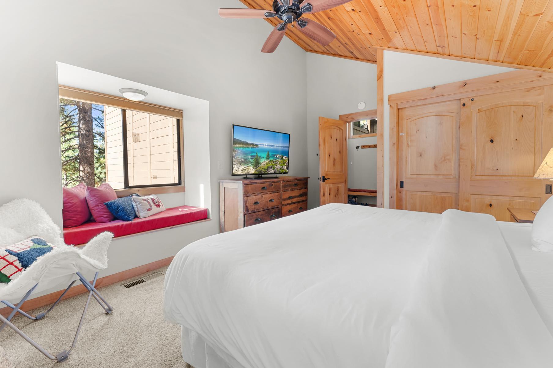 Cozy bedroom in Truckee vacation rental with wood accents, window seat, TV, and a ceiling fan.