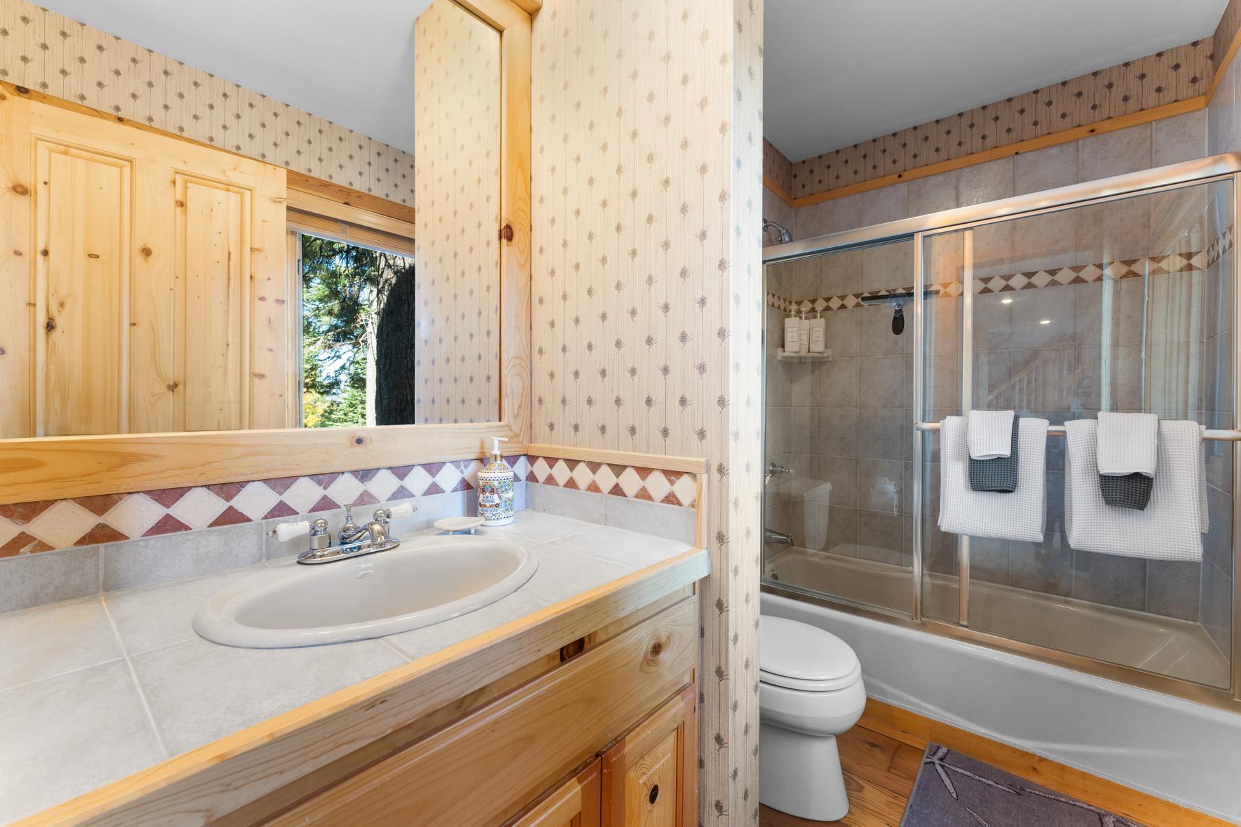 Cozy bathroom in a Truckee vacation rental, featuring a wooden vanity and tiled shower with glass doors.