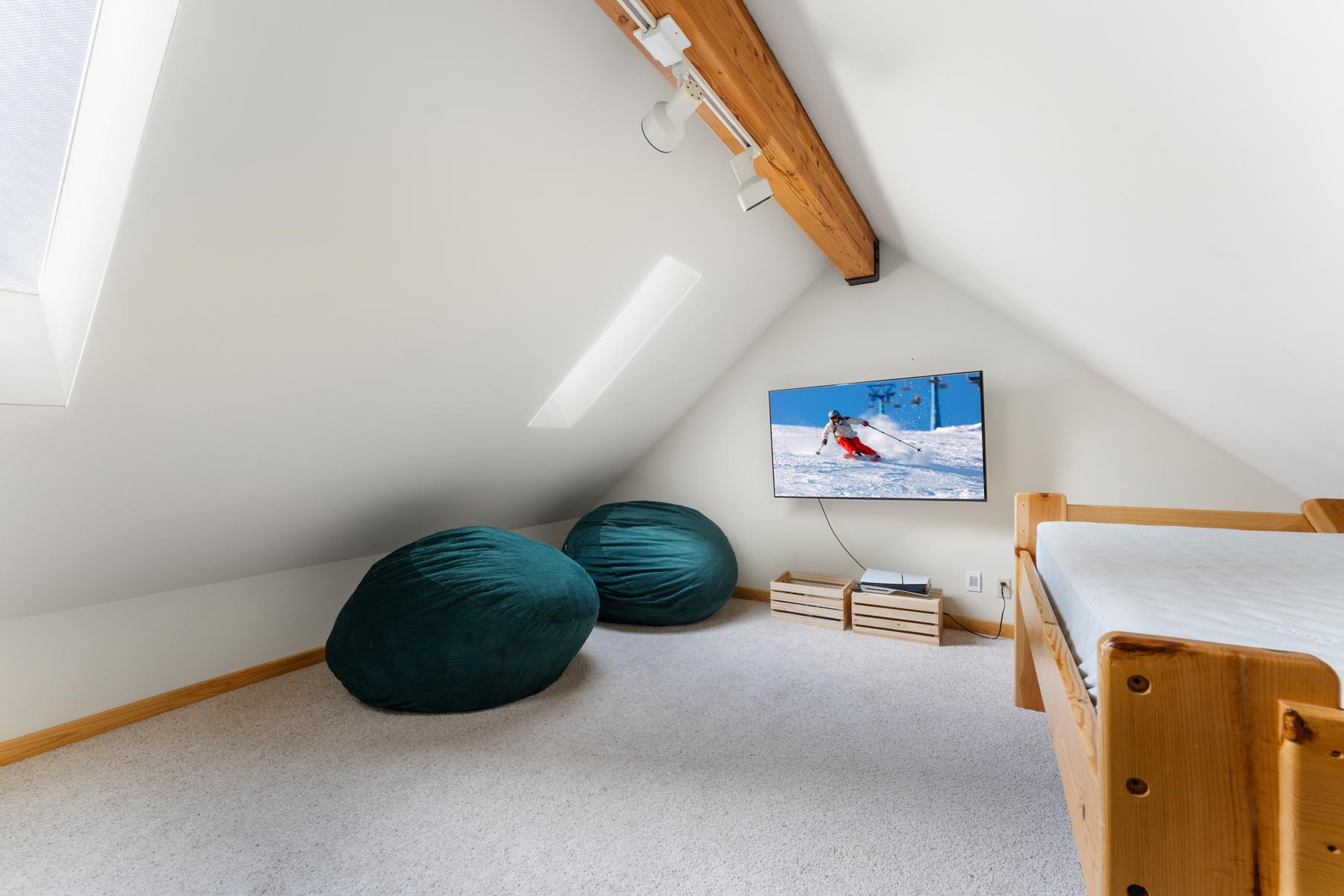 Cozy attic in Truckee vacation rental with TV, bean bags, and wooden bunk bed. Relaxing space with natural light.