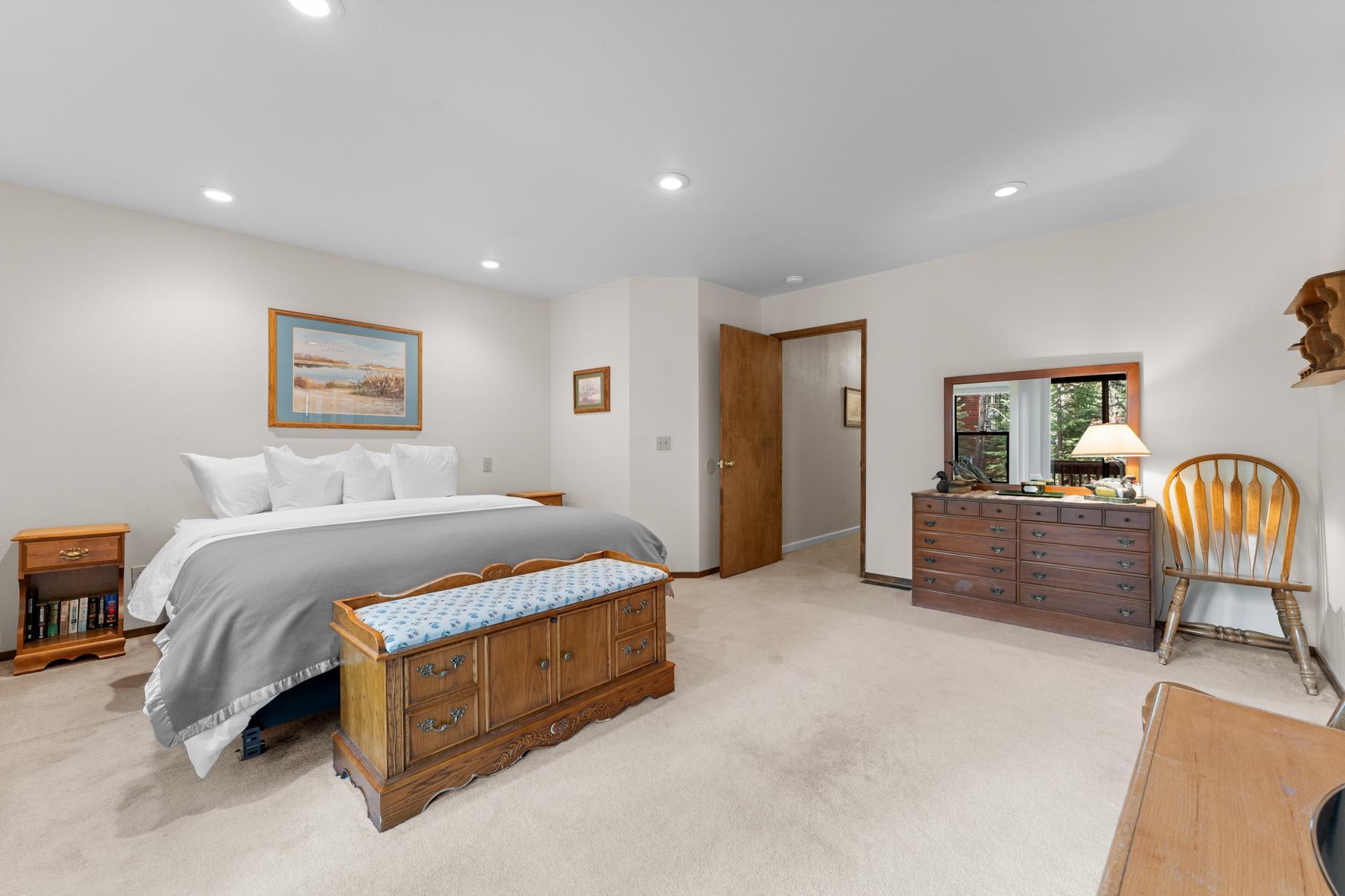 Spacious bedroom in a Truckee vacation rental with a cozy bed, wooden dresser, and a bench in a peaceful setting.