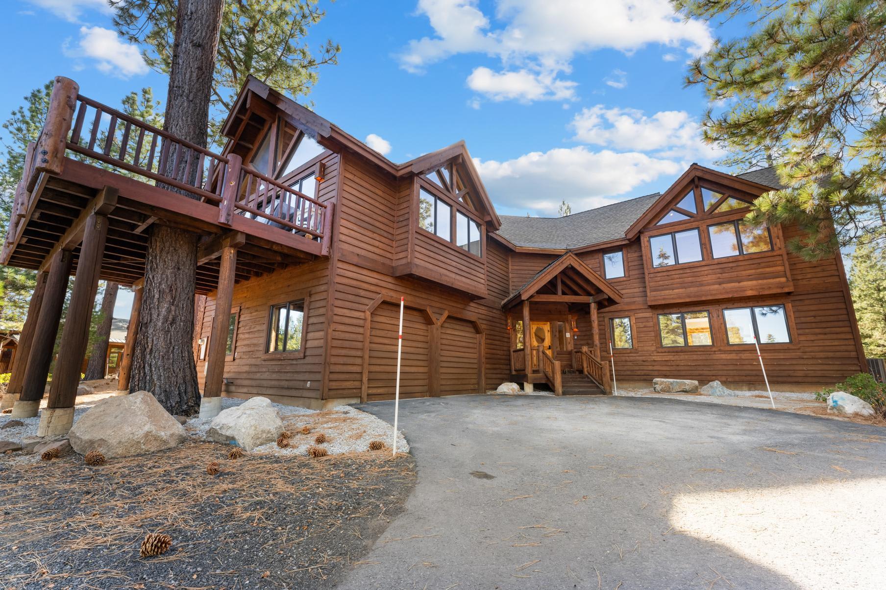 Rustic wooden vacation rental cabin in Truckee, surrounded by pine trees with a spacious driveway and large windows.