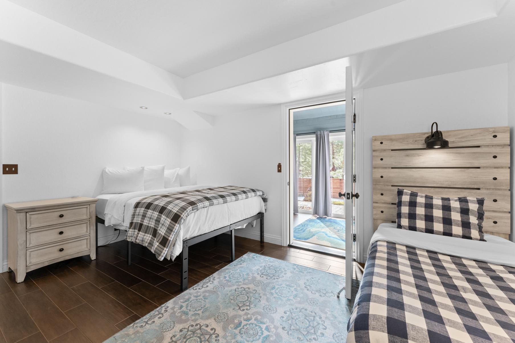 Bright bedroom in a Truckee vacation rental with two beds, plaid bedding, and a view of the patio through glass doors.