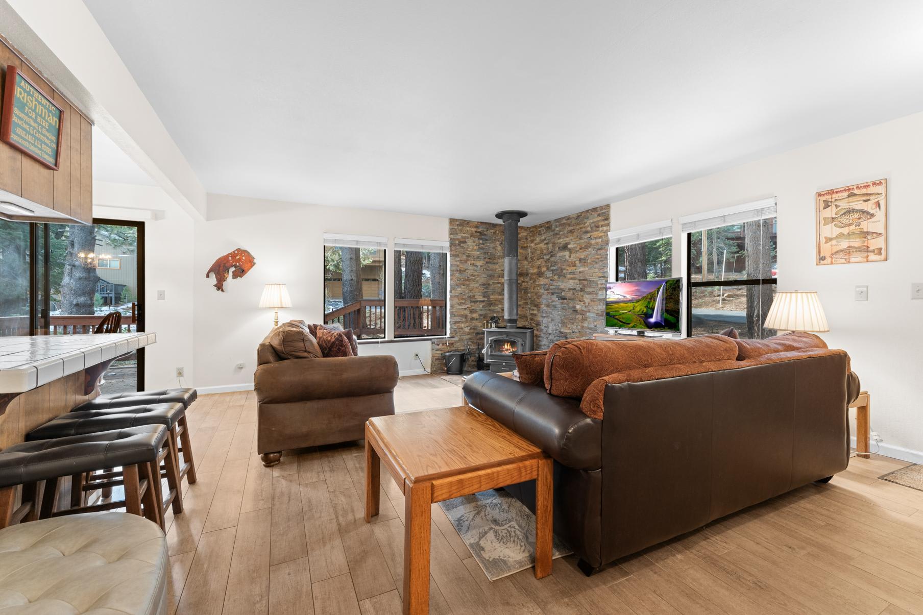 Cozy living room in Truckee vacation rental with a wood stove, leather sofas, and large windows overlooking the forest.