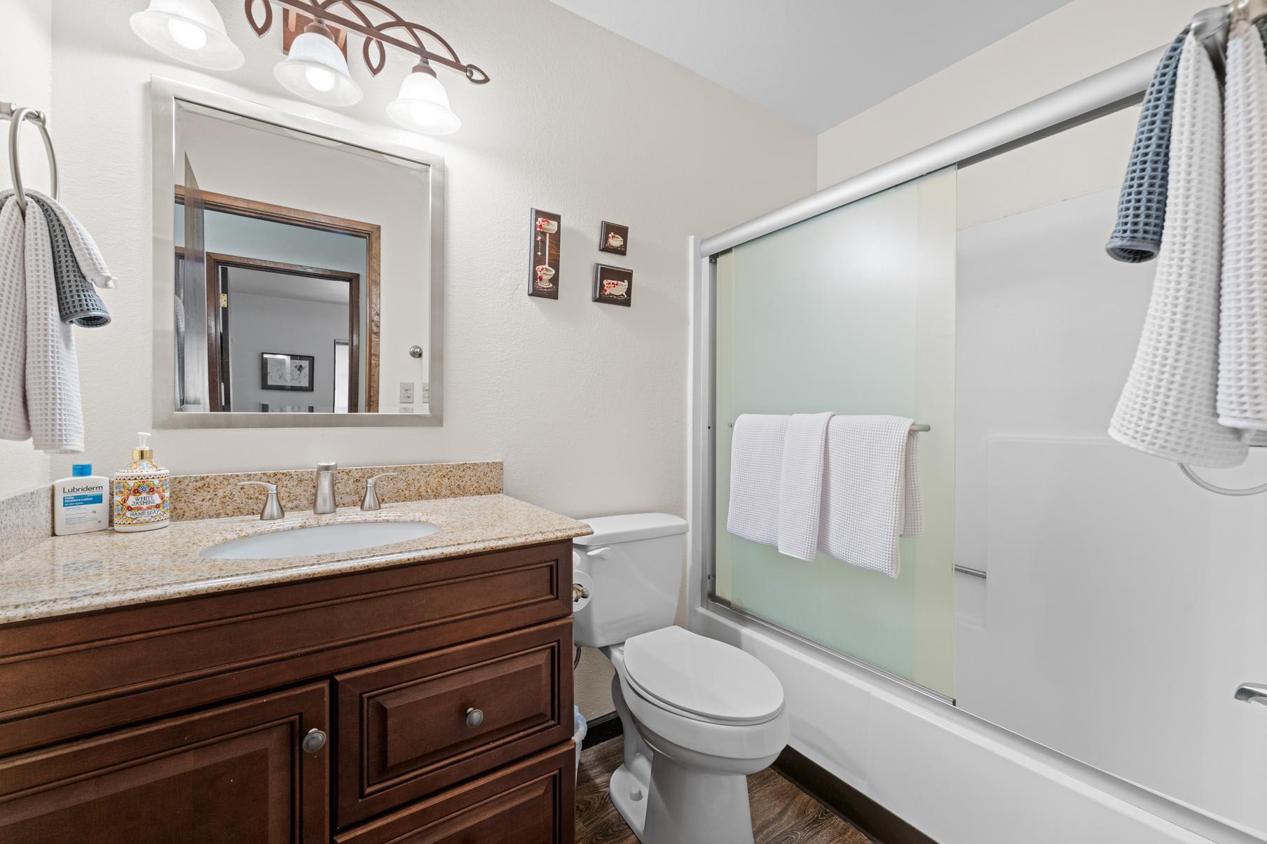 Modern bathroom in a Truckee vacation rental, featuring a granite countertop, wood vanity, and a glass-enclosed shower.