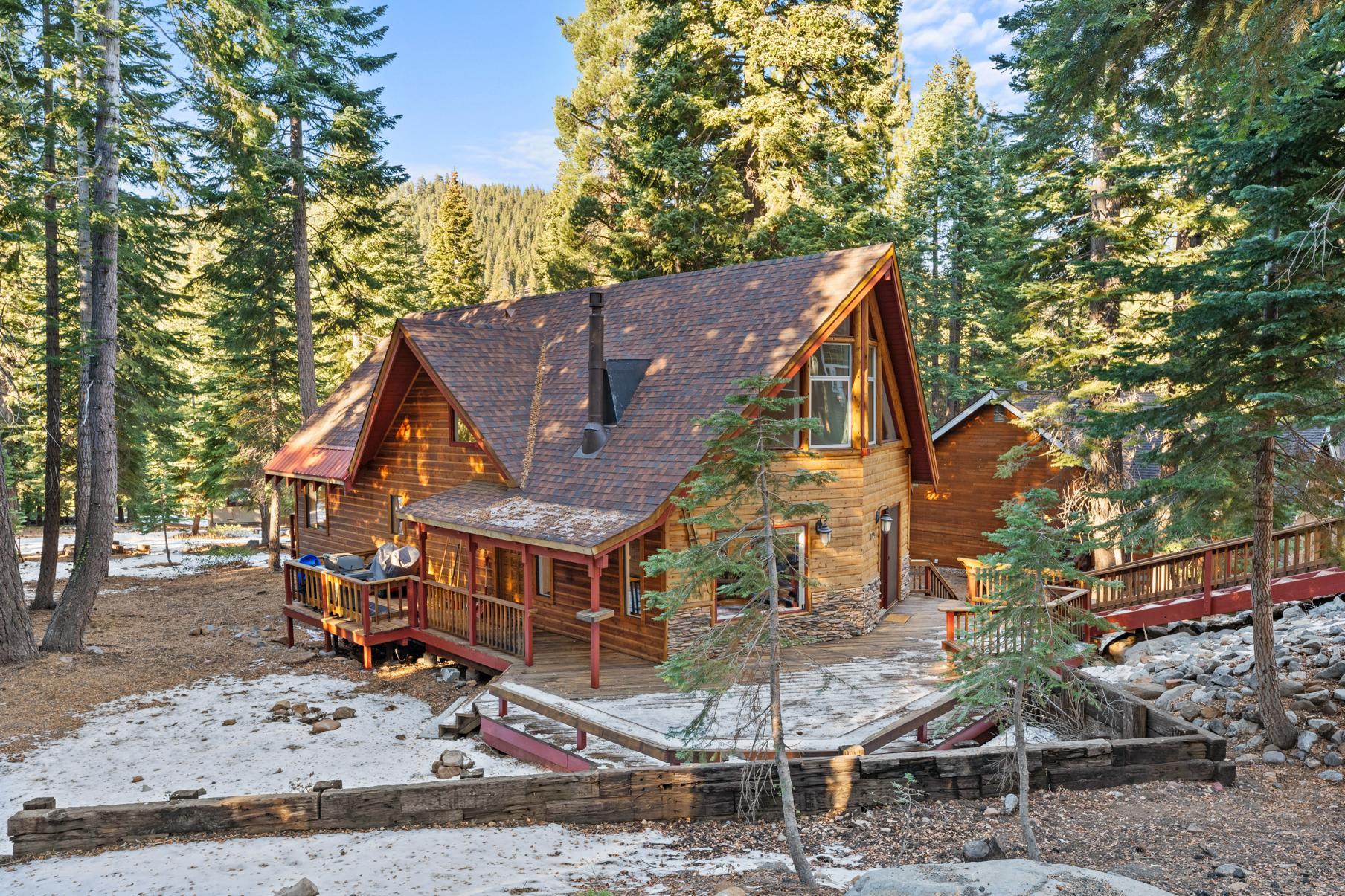 Wooden cabin vacation rental in Tahoe Vista, nestled among tall pine trees with patches of snow on the ground.