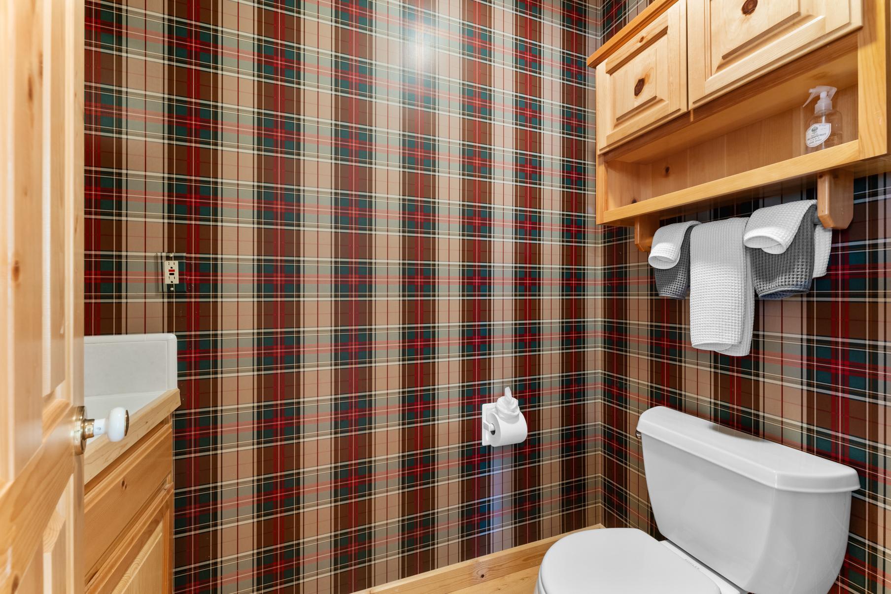 Bathroom in a Truckee vacation rental with plaid wallpaper and wooden cabinets.