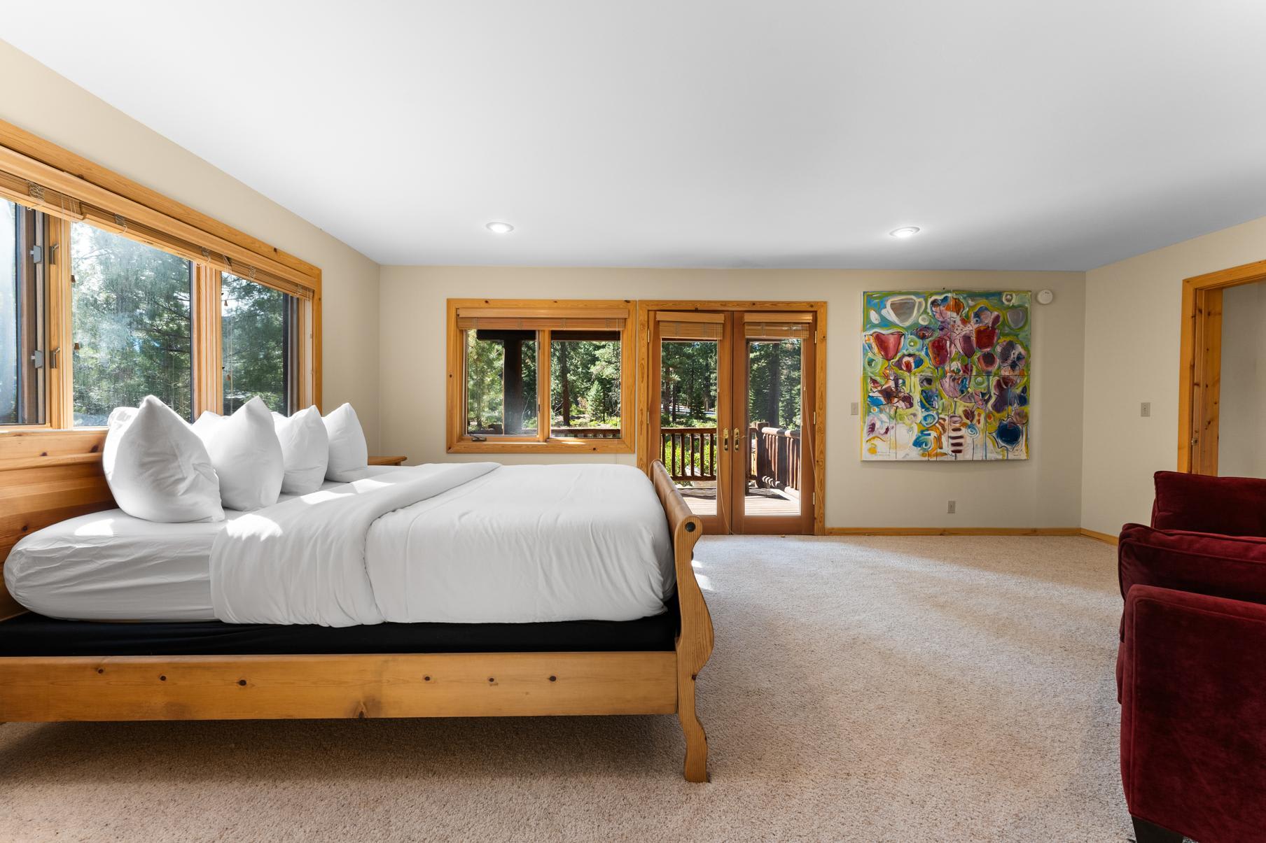 Spacious bedroom in a Truckee vacation rental with a large bed, modern art, and a view of the forest through glass doors.