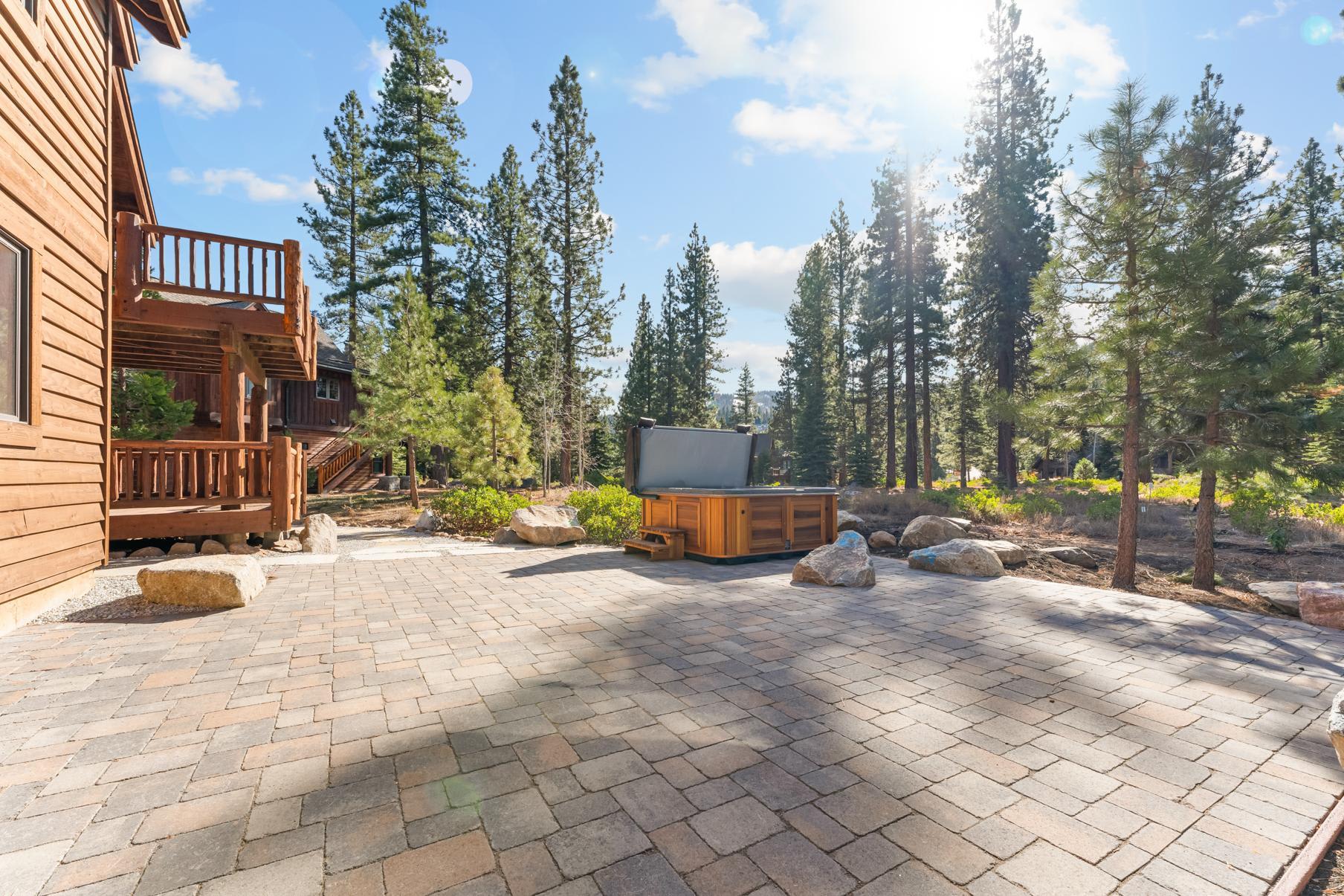 Sunny outdoor patio with hot tub at a Truckee vacation rental, surrounded by pine trees and natural scenery.