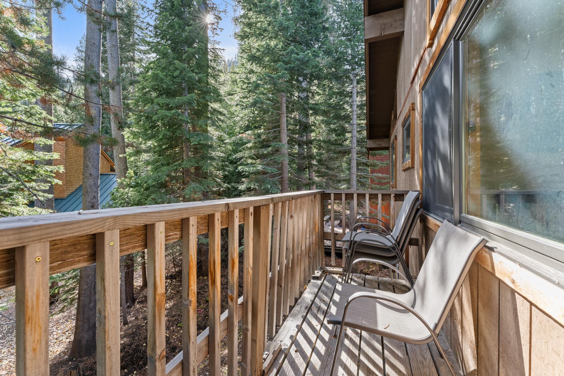 Truckee vacation rental balcony with chairs, surrounded by tall pine trees and sunny forest views.