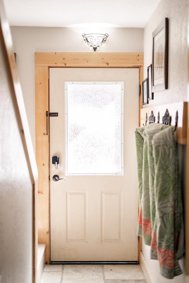 Bright entryway of a Truckee vacation rental with a wooden door, wall hooks, and colorful towels, lit by wall sconce.