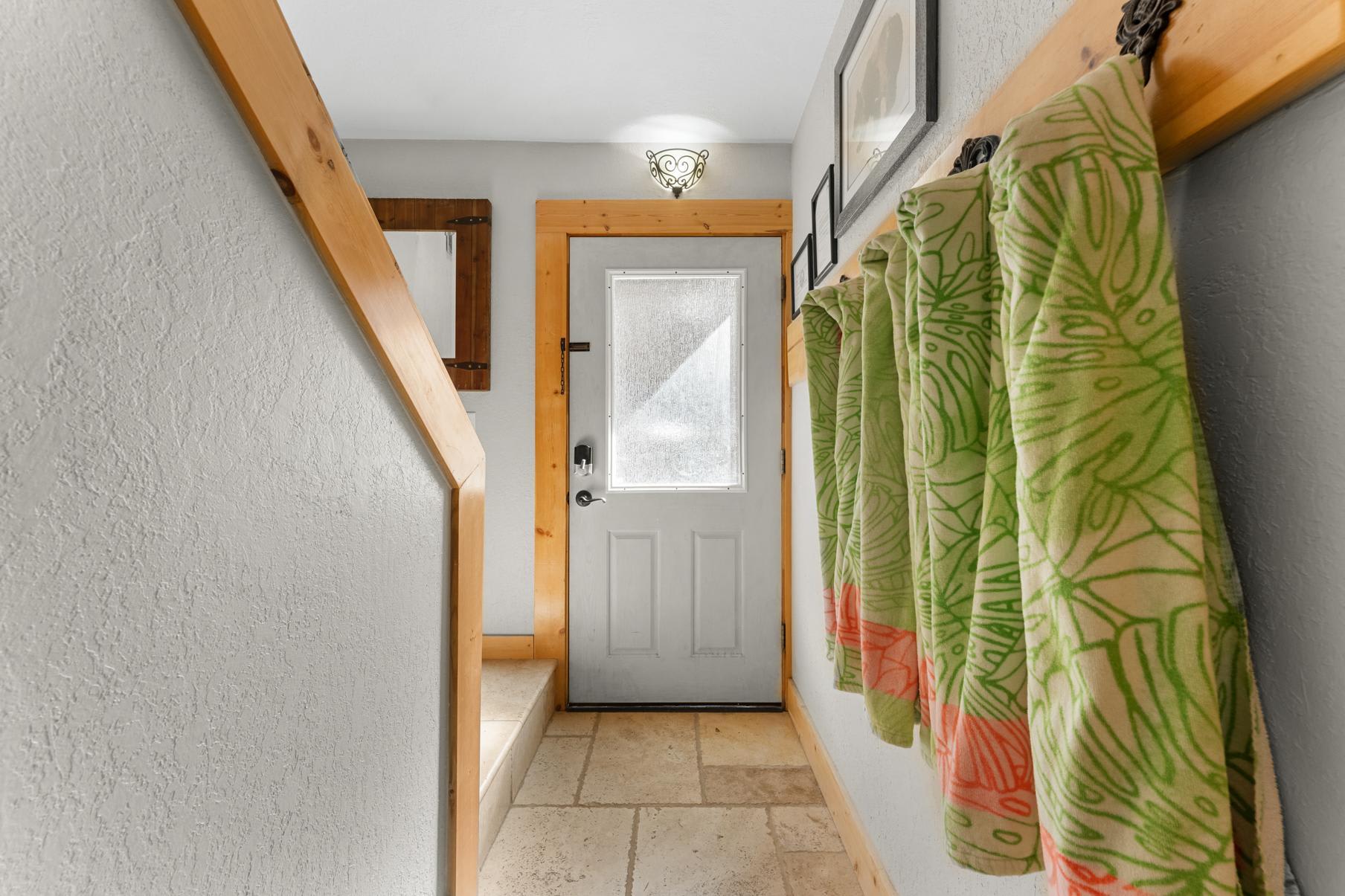 Entryway in a Truckee vacation rental, featuring a tile floor, light gray door, and decorative towels on wall hooks.