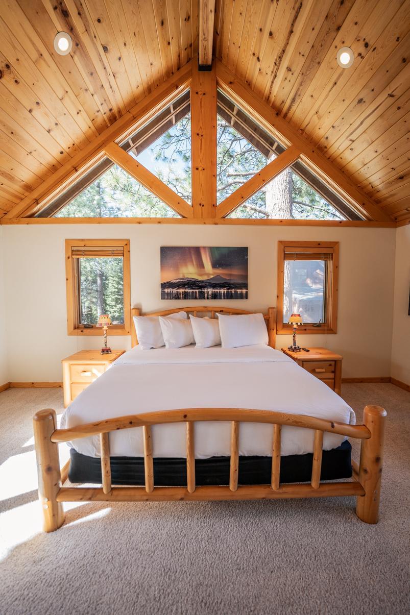 Cozy bedroom in a Truckee vacation rental with wooden beams, large windows, and a scenic forest view.