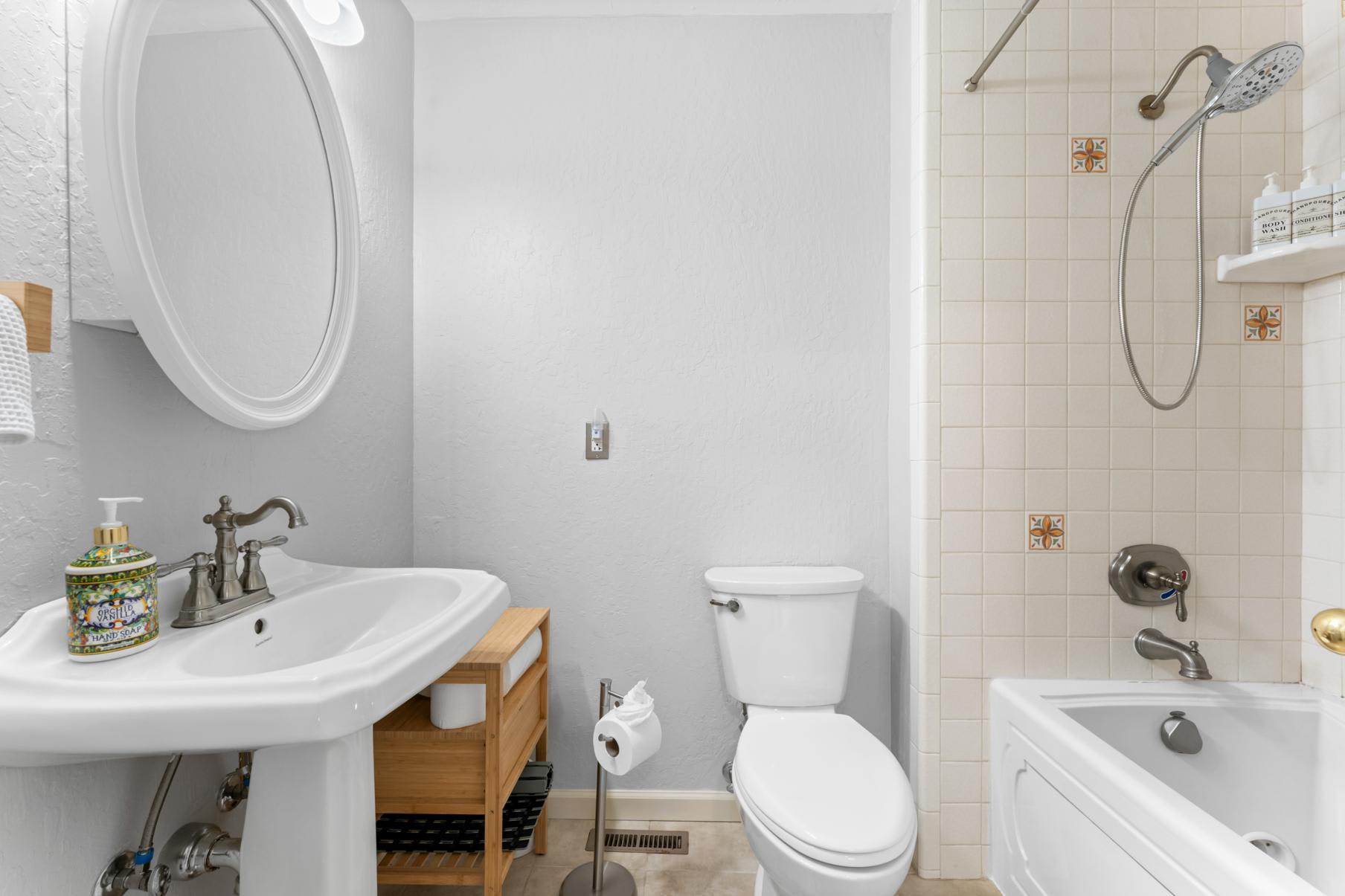 Modern bathroom in a Truckee vacation rental, featuring a pedestal sink, toilet, and shower-tub combo with neutral tiles.