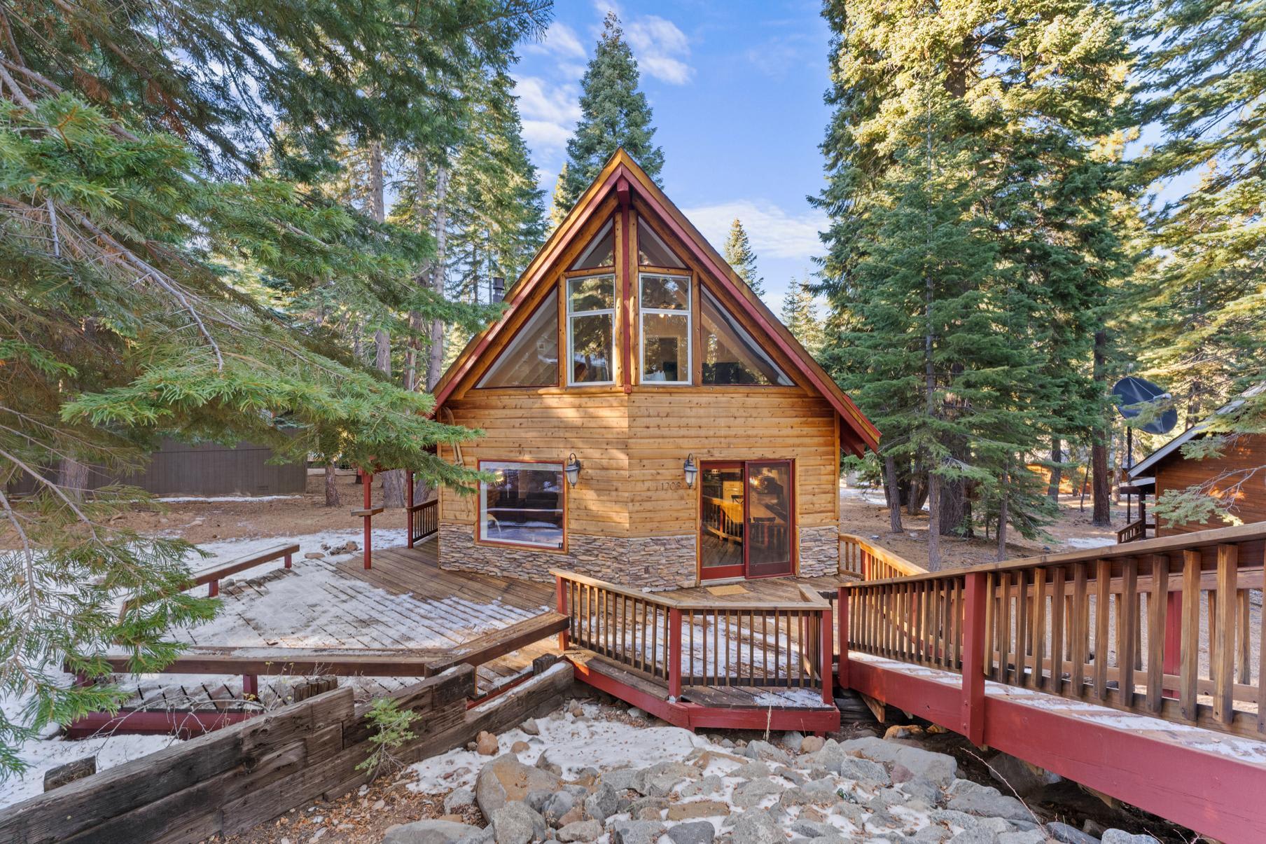 A-frame cabin vacation rental in Tahoe Vista with a wooden deck surrounded by pine trees and light snow on the ground.