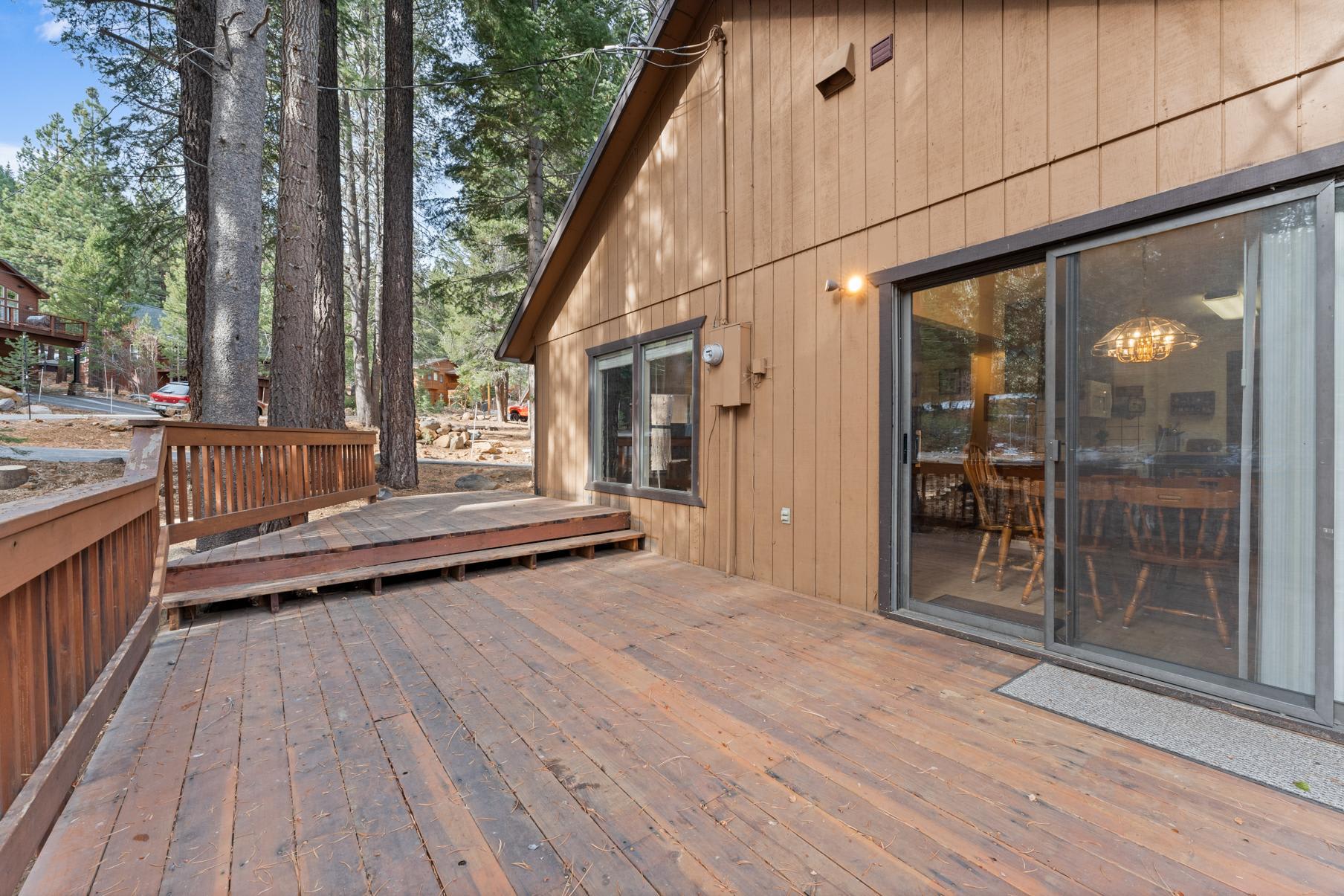 Truckee vacation rental with wooden deck, surrounded by tall trees, showcasing a cozy cabin-style exterior and sliding doors.