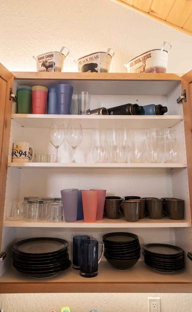 Open kitchen cabinet in a Truckee vacation rental with neatly arranged cups, glasses, and plates.