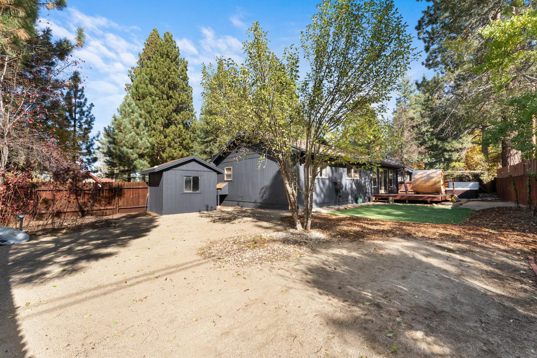 Backyard view of a vacation rental in Truckee, featuring trees, a wooden deck, and a small separate structure.