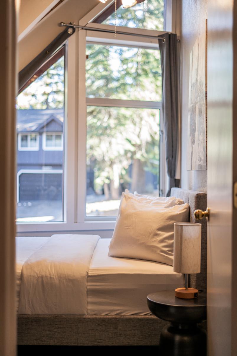 Cozy bedroom in a Tahoe Vista vacation rental, featuring a bed, soft pillows, and large window with scenic view.