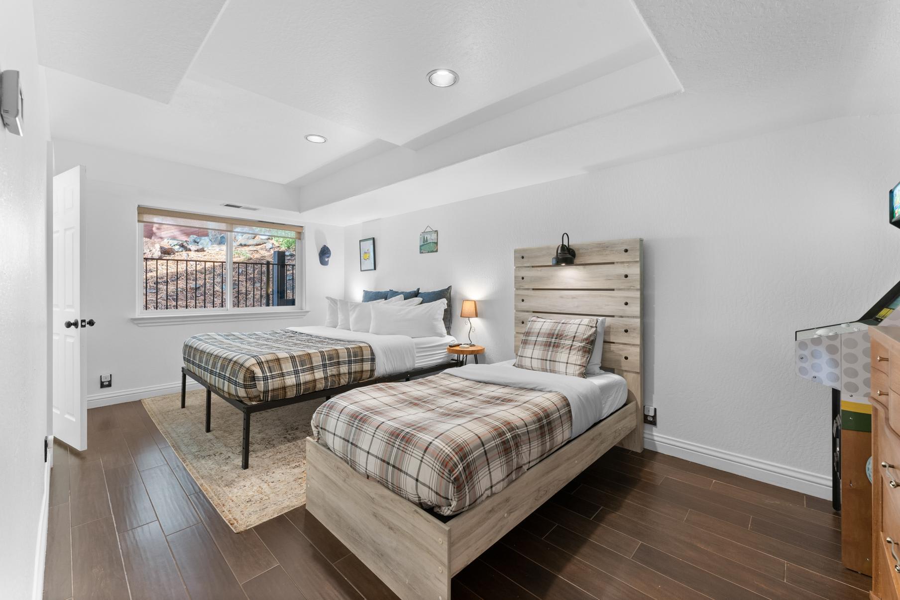 Cozy bedroom with twin beds and a game machine in a Truckee vacation rental, featuring wood floors and a large window.