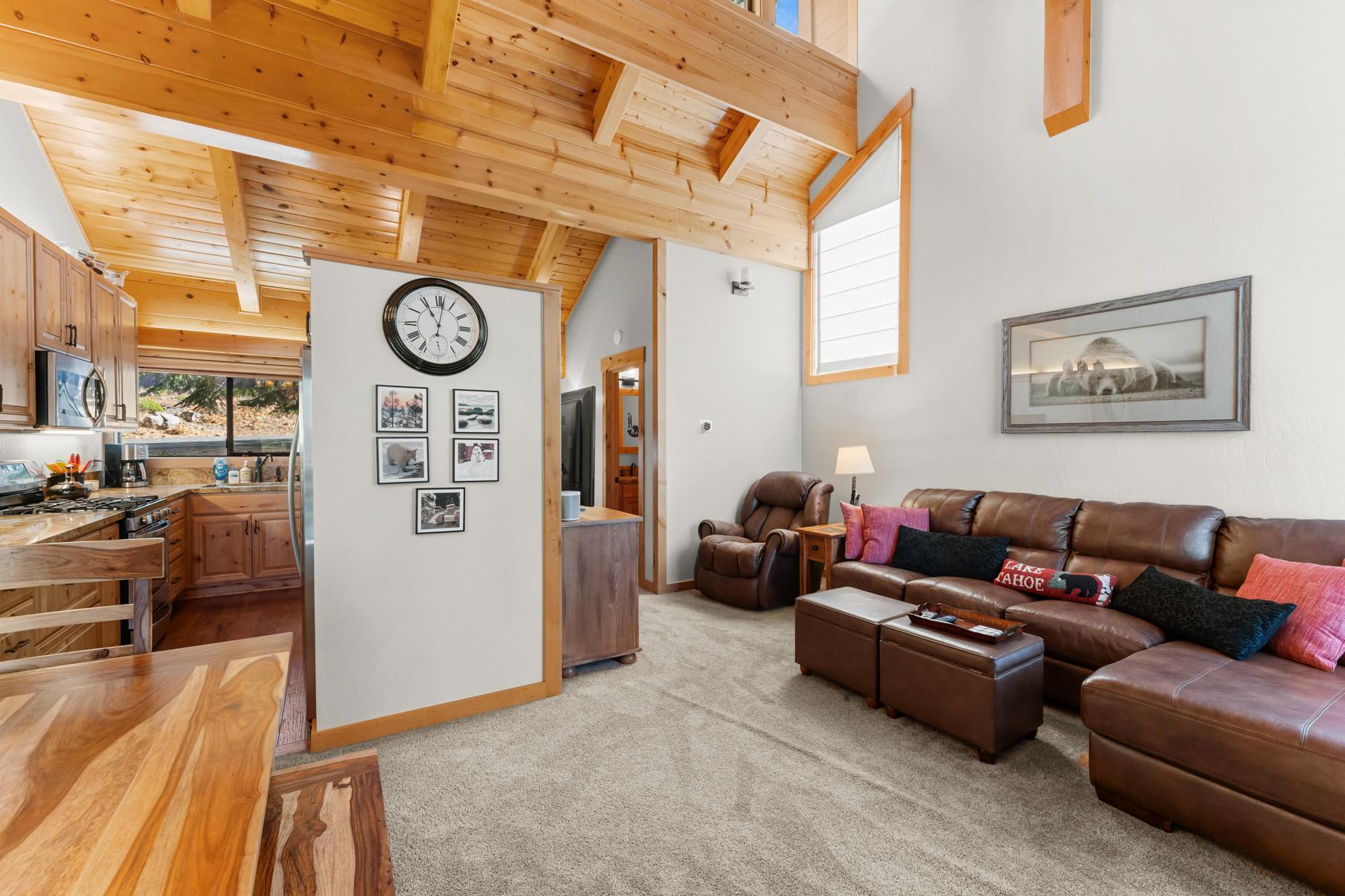 Cozy Truckee vacation rental with wooden beams, leather couch, kitchen, and natural light streaming through large windows.