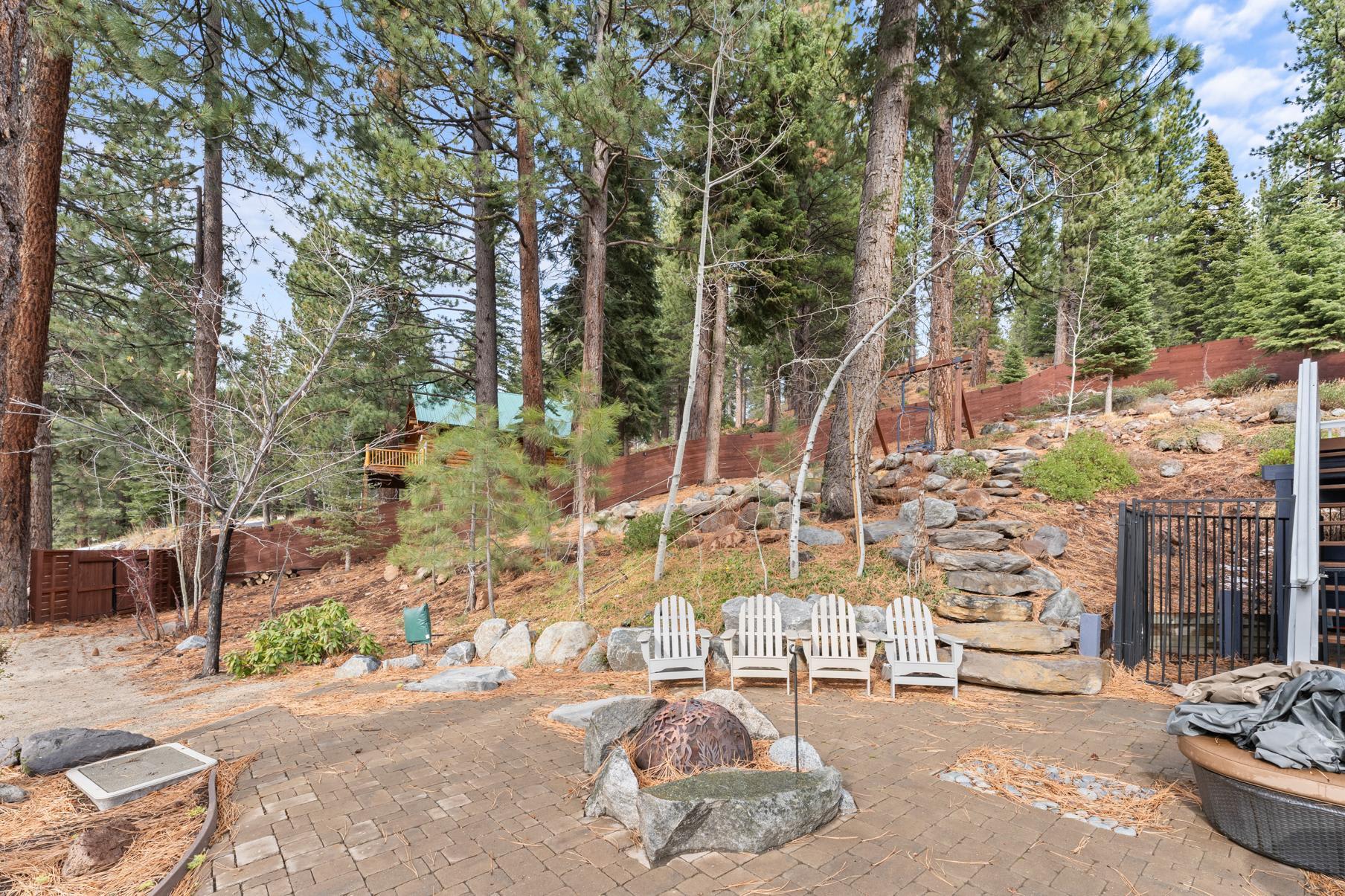 Forest view of a Truckee vacation rental patio with Adirondack chairs and a fire pit, surrounded by tall pine trees.