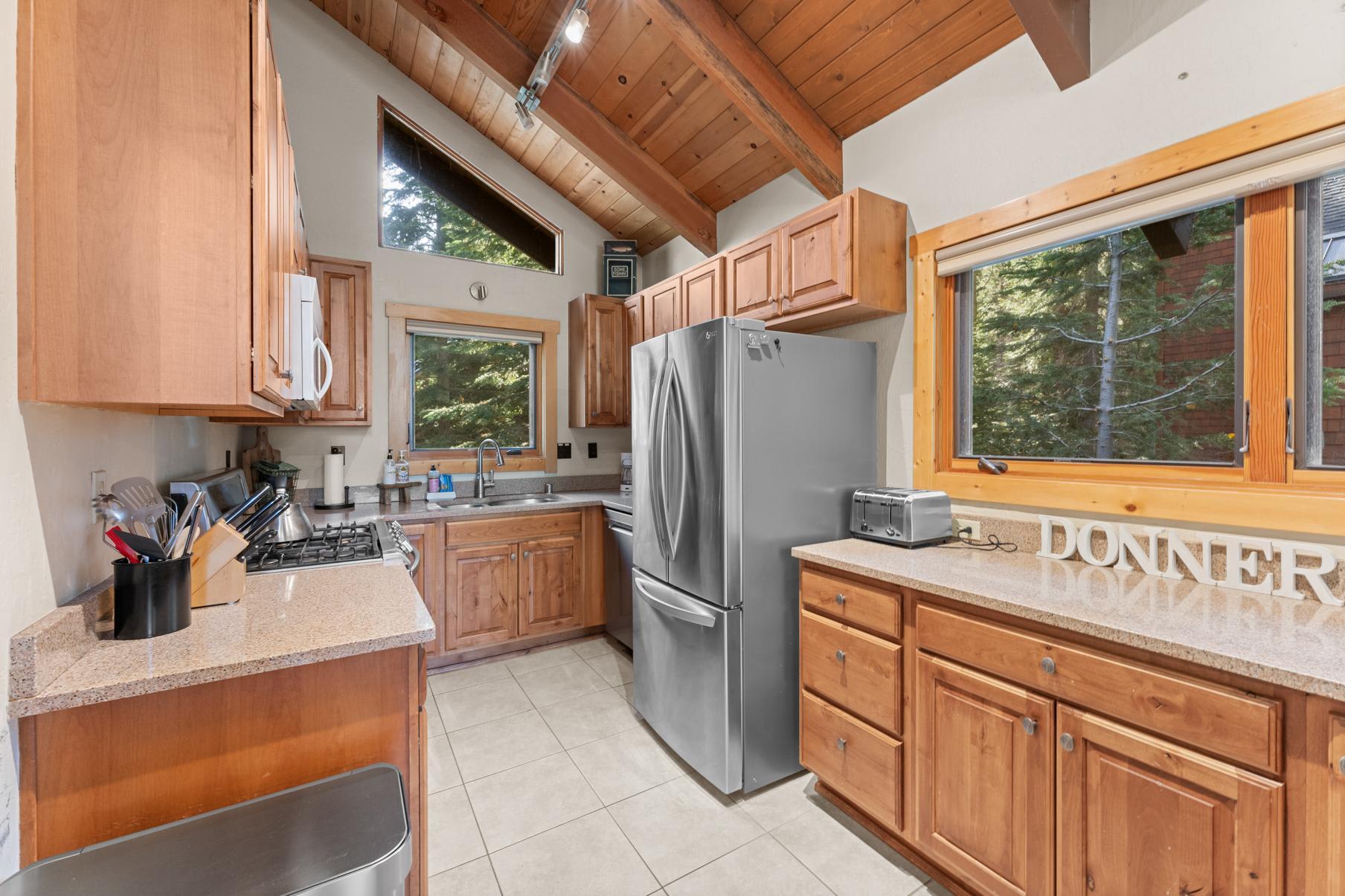 Cozy kitchen in a Truckee vacation rental with wooden cabinets, stainless steel fridge, and forest views through the window.